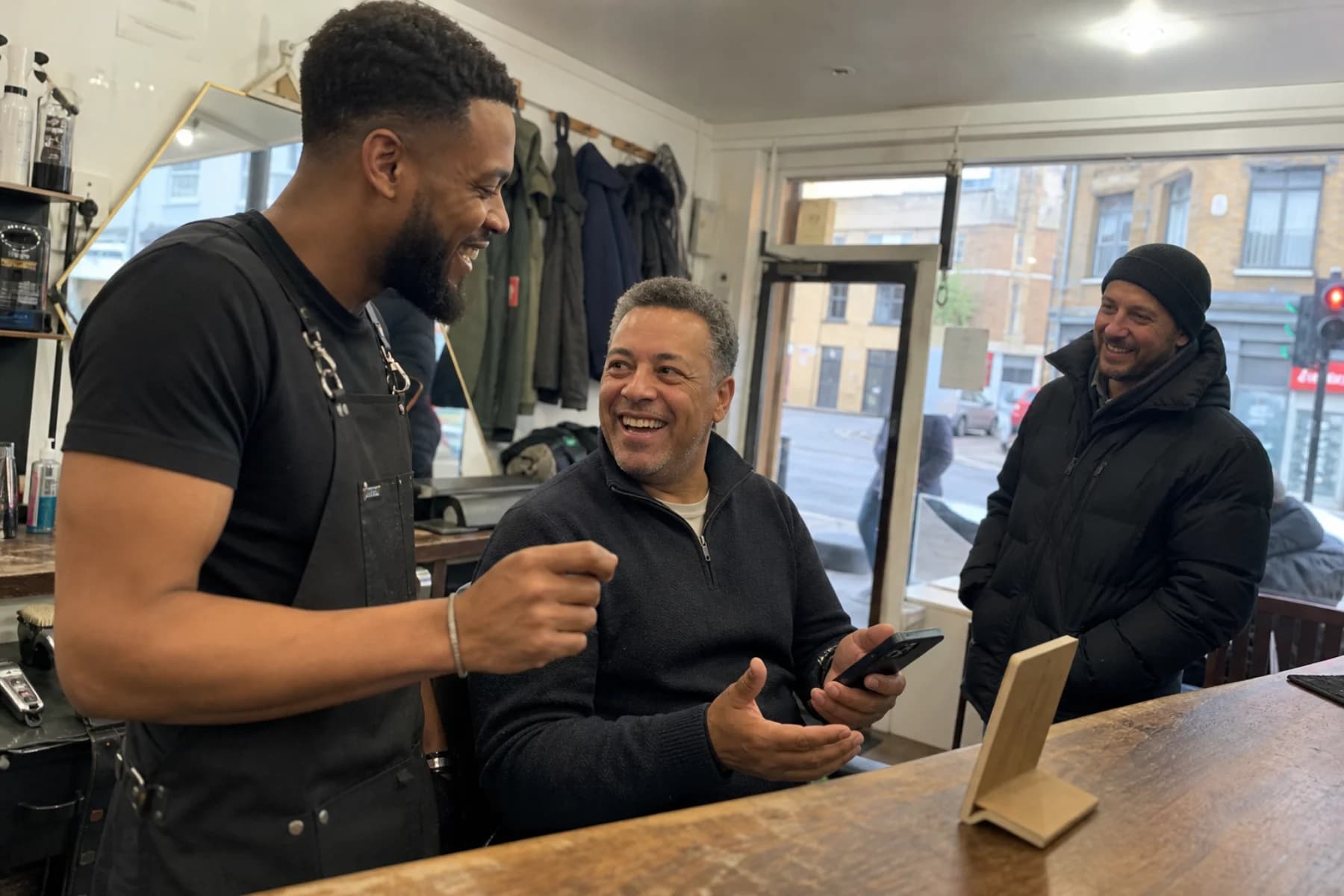 A neighbourhood barber laughing with two regular customers after a loyalty-card scan